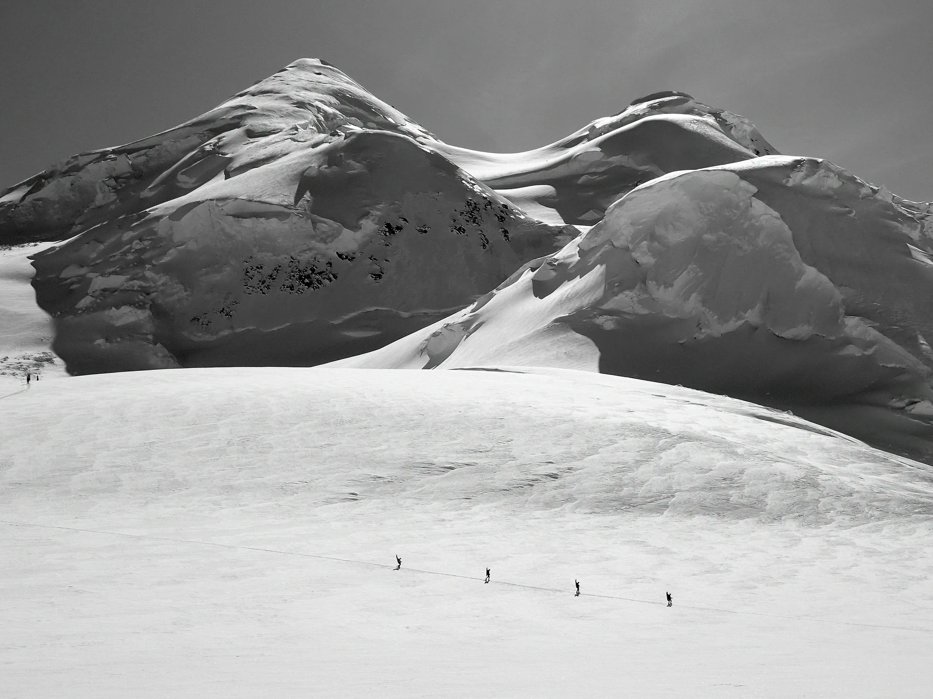 Four climbers roped together crossing a wide glacier below snow-covered domes